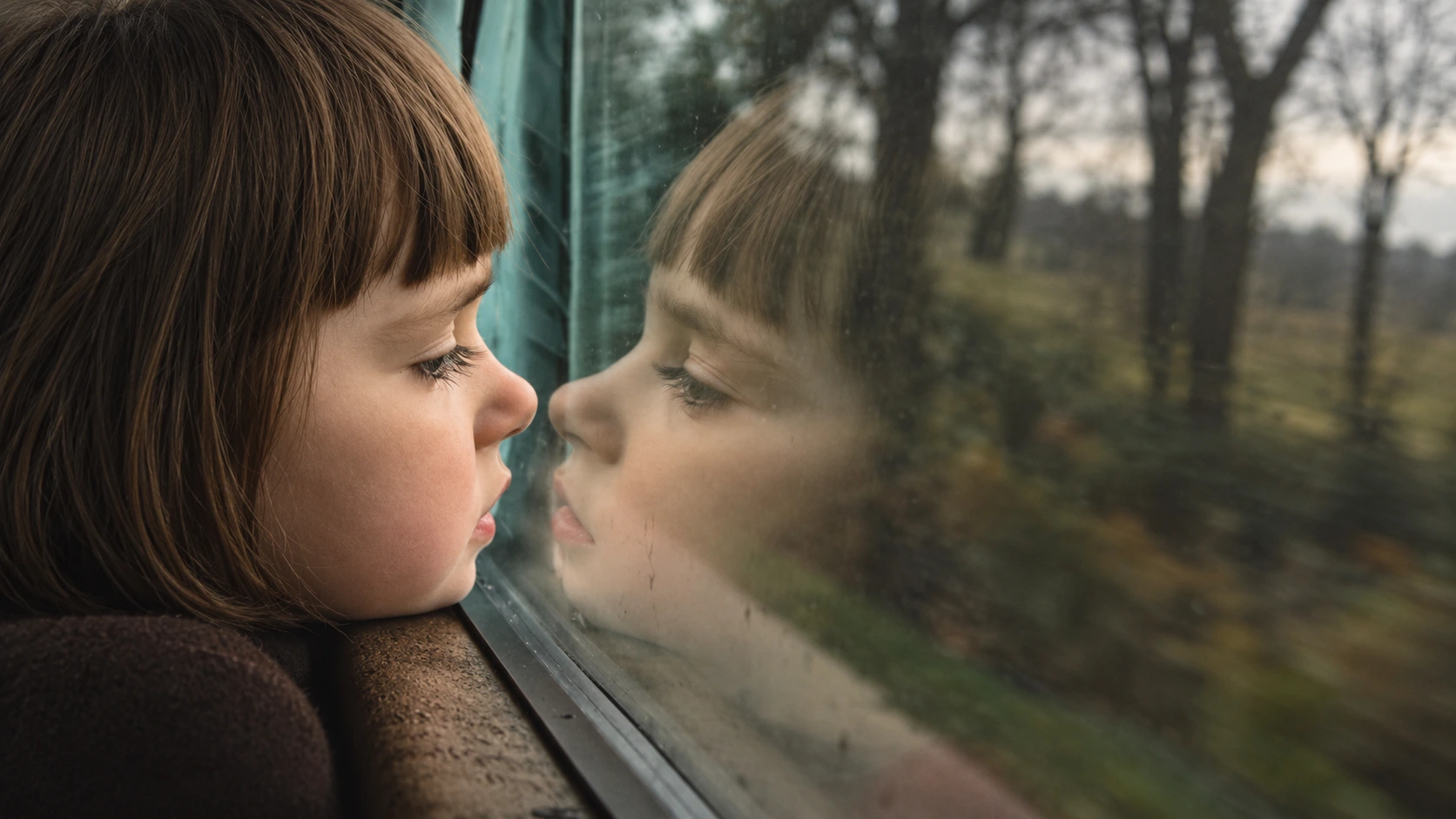 Child looking through a train window with a reflection in the glass