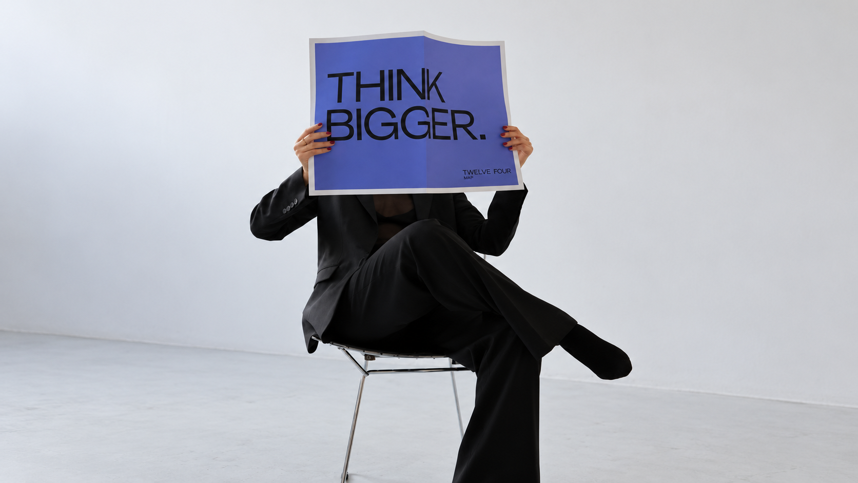 Person in a black suit holding a purple Think Bigger poster