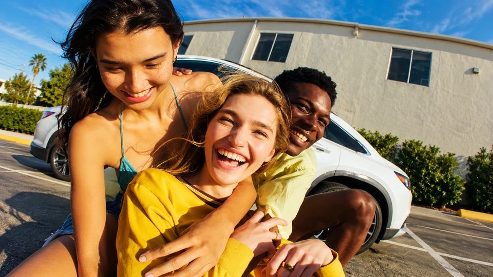 Three smiling friends sharing a group hug outdoors