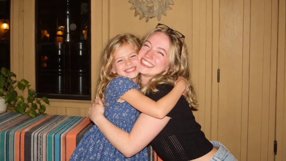 A smiling woman and a young girl sharing a hug indoors