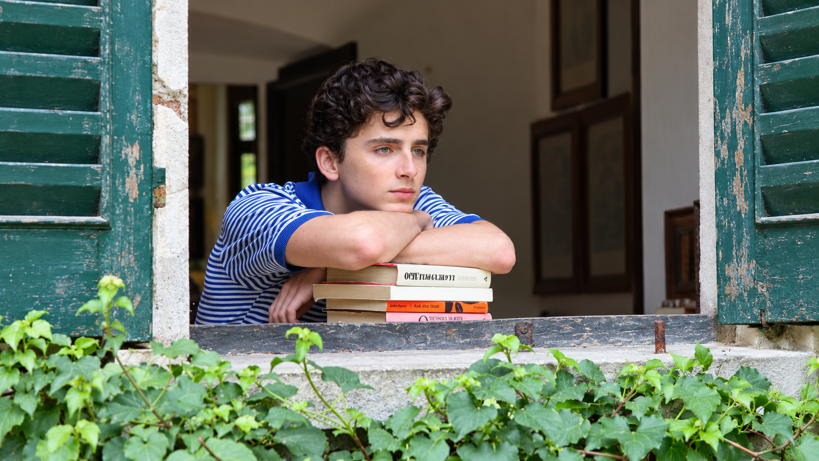 A young man resting on a stack of books by an open window
