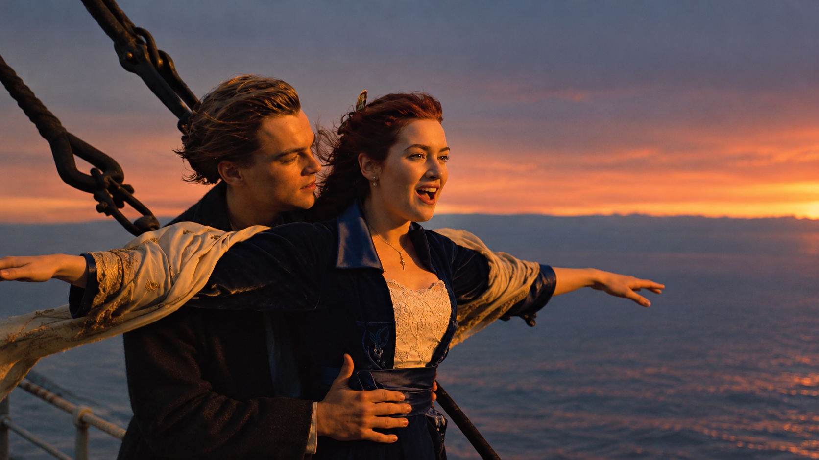 A couple on the bow of a ship at sunset