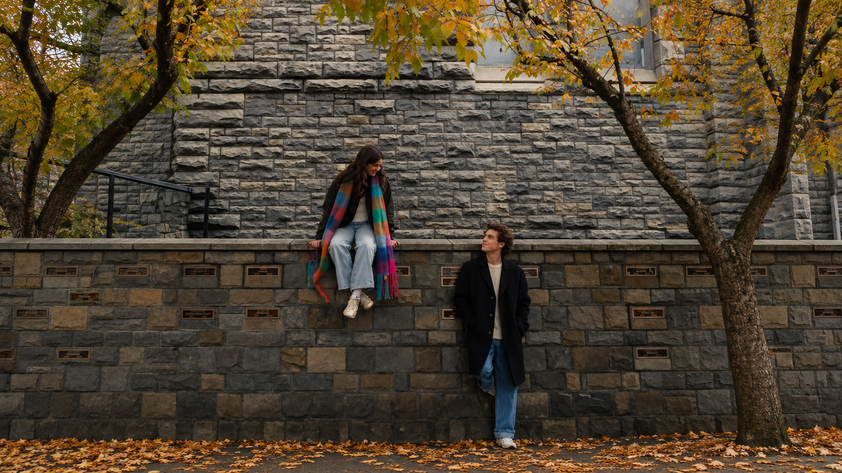 A couple beside a stone wall beneath autumn trees